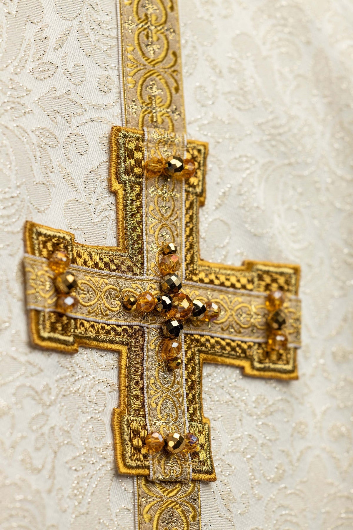 Ecru ornat na uroczystości eucharystyczne z przestrzennymi haftami krzyży i naturalnymi kamieniami, zbliżenie krzyża